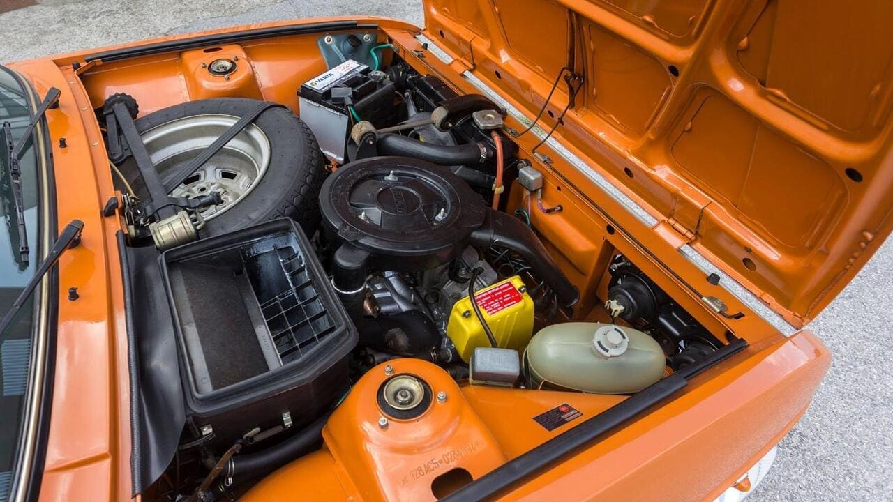 Wie im Lambor­ghini Miura versteift das Ersatzrad die Knautschzone, hier zwischen Spritzwand und Alu-Zylinderkopf. Dieser neigt sich um 20 Grad vor über die Zünd­- kerzen, Einlass- und Auslasstrakt beide hinten. Luftfilter- und Lüftungskasten auf der Beifahrer-, Getriebe auf der Fahrerseite. Spritzwasser aus dem Sack! Diese muntere Dreh- zahlorgienorgel passte auch als Mittelmotor in den X1/9.